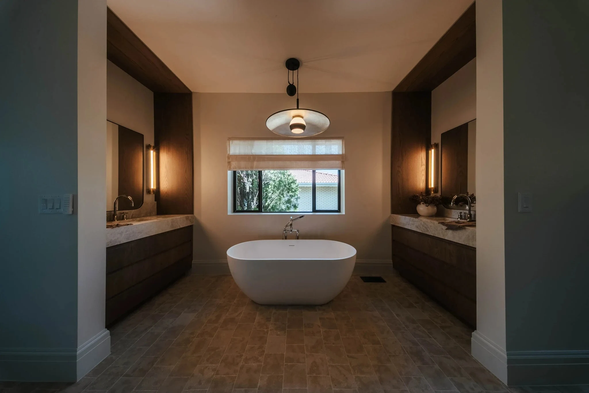 Freestanding bathtub between two dark wood vanities