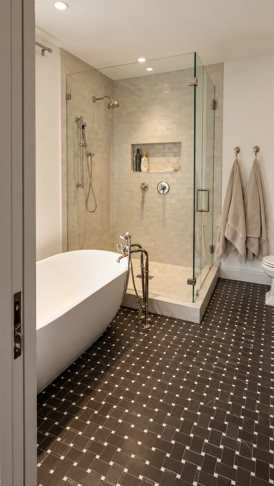 Freestanding bathtub beside a glass shower and dark patterned tile floor