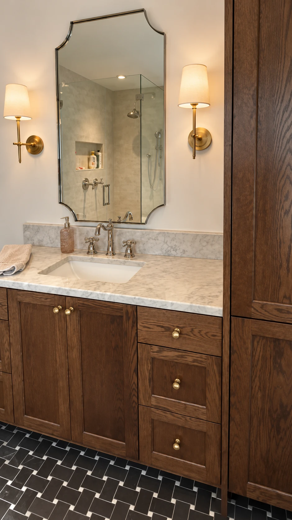 Dark wood vanity with marble countertop, shaped mirror, and brass sconces